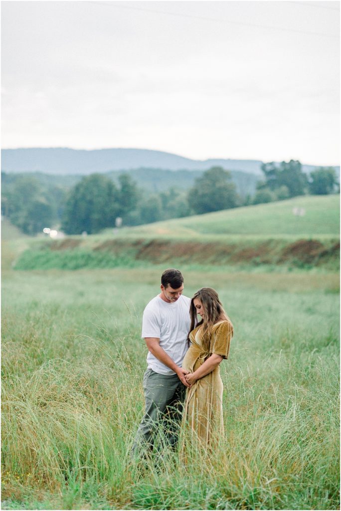 couple looking at baby bump in North Georgia with Mountains behind them